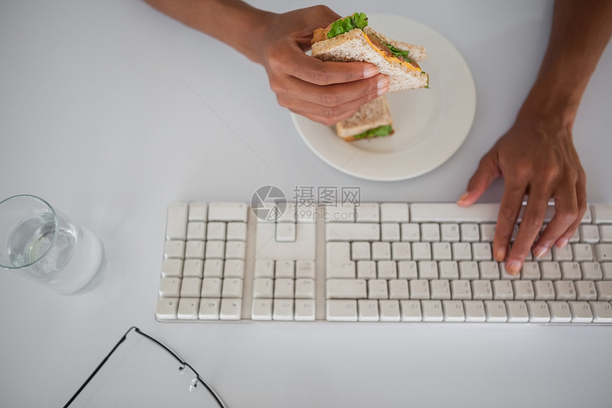 女商务人士在她桌子上吃三明治混血健康饮食午休食物职业女士商务盘子饮食办公室图片