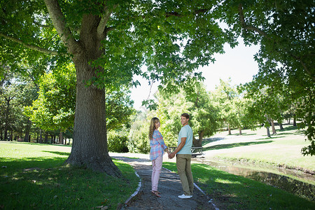 可爱的情侣在公园里手牵手行走女性女士亲密感男性太阳感情快乐男人微笑衬衫蓝天高清图片素材