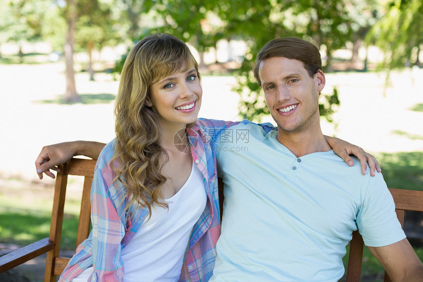 坐在公园的长椅上笑着看镜头的一对可爱情侣图片