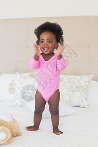 穿粉红婴儿裤的小女孩宝宝 站在床上玩具粉色家庭卧室女性幸福快乐动物棉被婴儿背景图片