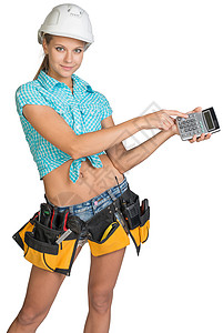 戴硬帽子和显示计算器的工具带的妇女工人工作室卡尺短裤微笑评价维修员工层面牛仔裤背景图片