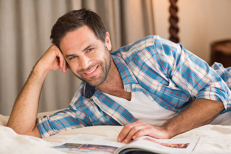 帅哥在床上看书的杂志上放松闲暇卧室公寓家庭生活微笑快乐房子住所家庭男性背景图片