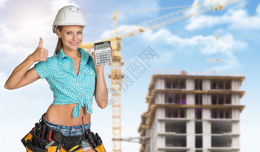 带着计算器的硬帽子微笑着年轻女子工程项目牙齿工具安全帽蓝衬衫蓝天建筑黄色工业背景图片