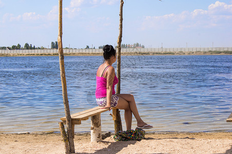 年轻女人坐在长椅上看着大海晴天女孩地平线海滩闲暇蓝色女性假期天空海岸夏天高清图片素材