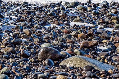 海滩岸边有泡沫的石头背景图片