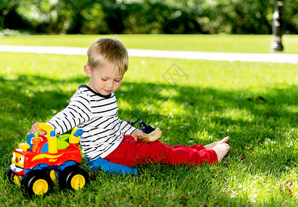 小学龄前男孩在城市公园玩大玩具车户外的高清图片素材
