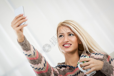 美丽的女孩自取自我水平女子杯子自拍乐趣微笑幸福手机金发女郎背景图片
