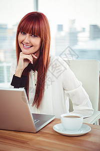 使用笔记本电脑微笑时装女商务人士女性刘海职场咖啡红发潮人边缘桌子技术热饮背景图片