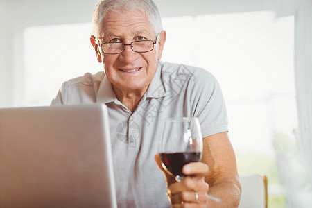 使用笔记本电脑和喝酒的专注老人男人技术酒精头发房子眼镜老年公寓闲暇酒杯背景
