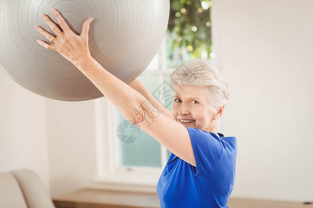 高级女性在锻炼时举起球休闲训练起重老年人头发力量公寓退休女士房子背景图片
