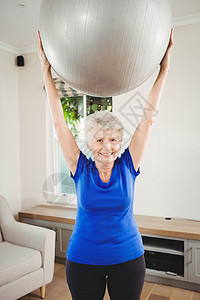 高级女性在锻炼时举起球运动力量微笑健身女士退休公寓服装老年头发背景图片