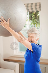 高级女性在锻炼时举起球头发力量健身健身房女士沙发休闲运动公寓拉伸背景图片
