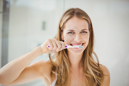 青年妇女刷牙浴室长发微笑女性浅色口腔打扫医疗健康牙刷背景图片