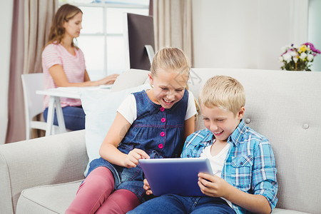 儿童使用数字平板电脑 而母亲在背景中沙发高清图片素材