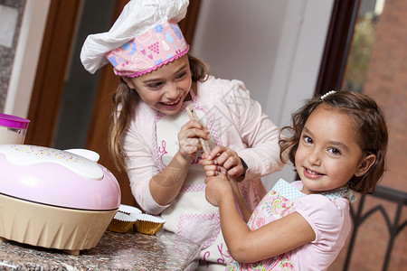 两个小女孩 一起准备蛋糕纸杯蛋糕厨房微笑姐妹厨师乐趣围裙背景图片