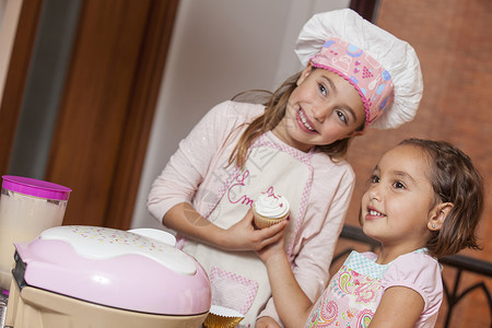 两个小女孩 一起准备蛋糕纸杯蛋糕厨房厨师乐趣姐妹围裙微笑背景图片