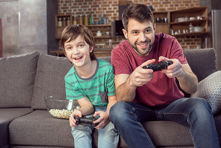 少年时代微笑的父亲和儿子在家玩电子游戏背景