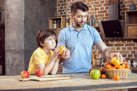 少年时代父亲和儿子在厨房餐桌上从篮子中挑选水果背景