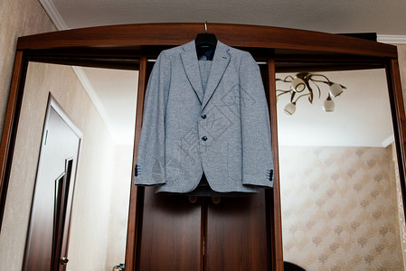 西装剪裁美丽的灰色新郎的西装挂在房间里衣柜上套装服装婚礼织物棉布燕尾服男人服饰按钮衣架背景