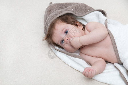 替牙期可爱的小宝贝女孩躺在白色的毯子上 嘴里含着手指 快乐的童年概念 婴儿吮吸手指看着你 三个月大的小孩嘴里含着手指躺着背景