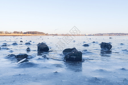 冰冻湖上冰雪中的黑岩石背景图片