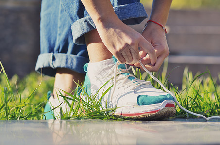 身着牛仔牛仔裤 鞋带和鞋带的年轻女孩站在绿草地一旁观看近距离青菜季节花边学生领带男人公园造型女性运动背景图片