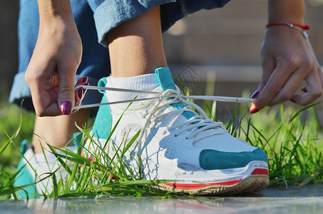 身着牛仔牛仔裤 鞋带和鞋带的年轻女孩站在绿草地一旁观看近距离公园学生青菜女士花边女性领带运动季节造型背景图片