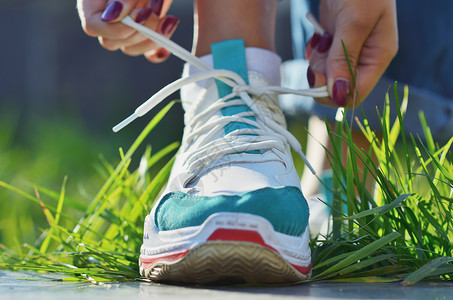 年轻女孩用鞋带系着运动鞋的鞋带 站在绿草地近视下背景图片