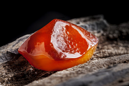 天然琥珀 一块黄色和红色半透明的天然琥珀 放在一块石头上琥珀色抛光地质学珠宝太阳石宏观蜂蜜反射宝石化石背景图片
