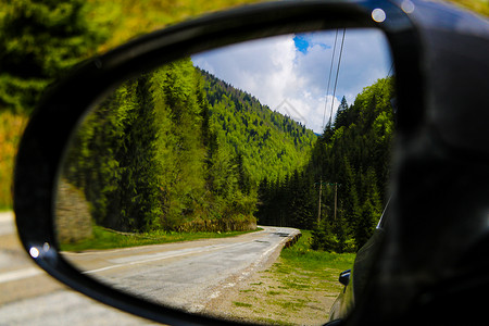 在阳光明媚的一天看到一条山路和一片森林 反射出一辆汽车镜子 失去焦点背景
