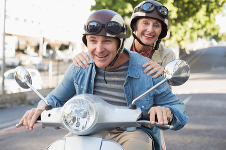 快乐的成熟情侣在城里骑摩托车助力车女士女性男性感情交通金发乐趣金发女郎车辆背景图片