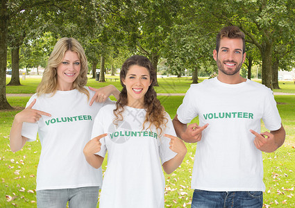 志愿人员用数字复合体指着他们的衬衣草地志愿者社区服务机构手指朋友们帮助青年树木背景