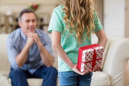 女孩在客厅里拿着给父亲的惊喜礼物家庭喜悦礼物盒家庭生活眼睛男人服装沙发公寓住所背景图片