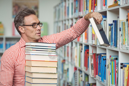 细心的学校老师在图书馆拿书男性工作服装专注知识平衡男人智力书柜书架背景图片