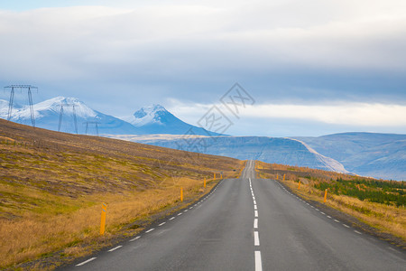 冰岛的公路路由空洞铺面道路通向山上 下雪覆盖在电线旁的小提示背景图片