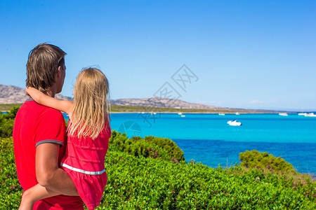 年轻的父亲和他的小女儿在撒丁岛欣赏碧绿的大海美景爸爸孩子海岸假期海滩享受父母热带喜悦游客女孩高清图片素材
