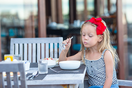 可爱的小女孩在户外咖啡厅早餐时吃粥芒果高清图片素材