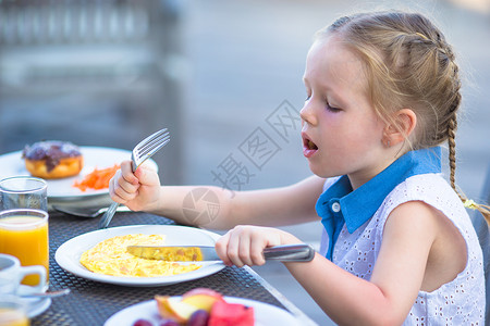 可爱的小女孩在户外咖啡厅吃早餐水果橙子婴儿餐厅眼睛小吃快乐杯子西瓜金发夏天高清图片素材
