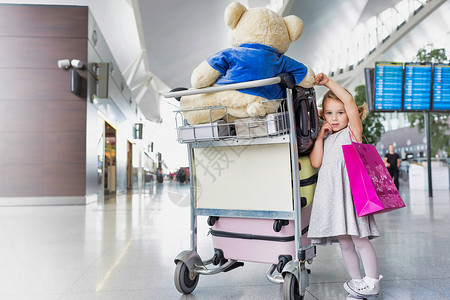 坐在行李车旁边的可爱小女孩肖像 她们带着手提箱在机场上背景图片