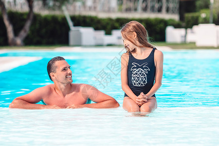 母亲和小女儿的家庭在豪华游泳池中享受暑期假期男人闲暇女孩身体成人蓝色黑发娱乐活动热带背景图片