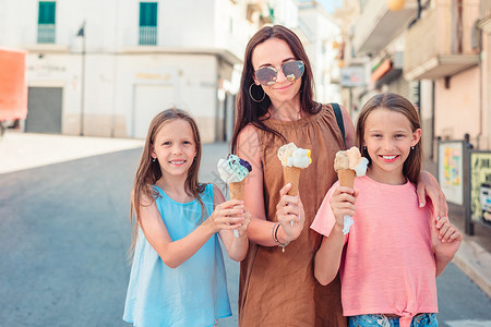 吃冰淇淋女孩母亲和可爱的小女儿 在户外吃冰淇淋食物餐厅父母孩子城市奶制品公园女孩喜悦享受背景