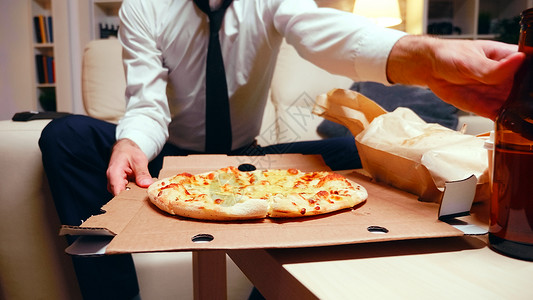 下班一一整天 商务人士带着比萨饼回家吃披萨男人垃圾食物渠道遥控商务套装交换客厅外卖背景图片