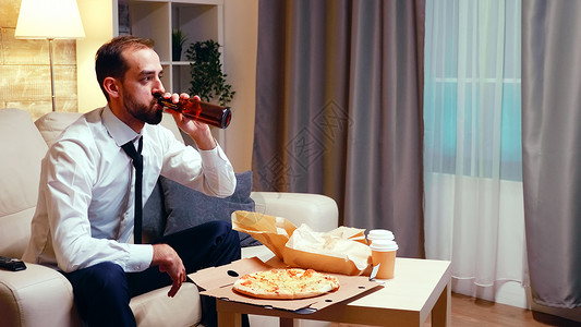 在沙发上休息的商务人士 喝啤酒吃披萨领带食物客厅外卖程序人士企业家工作食品啤酒背景图片