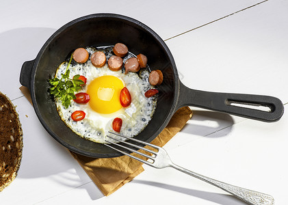 炸鸡蛋和香肠片 在圆黑色的黑铁煎饼背景图片
