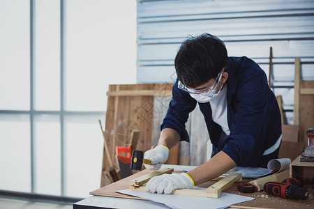 亚洲男木匠在家里用木工工具和木头在车间里处理技术图纸或蓝图建筑纸木板制作者工艺工匠工作职业男性房子作坊男人工人高清图片素材