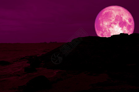 满粉红色月亮背面的太阳光环绕着海岸的岩石山背景图片