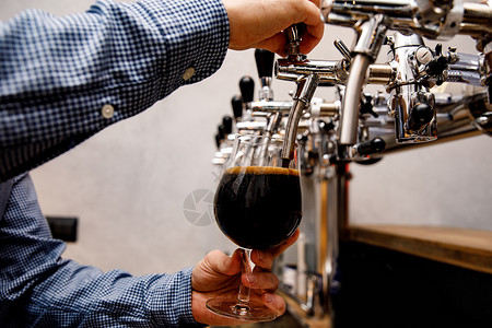 酒保在酒吧里从水龙头上倒新的黑啤酒派对草稿啤酒酒精服务员调酒师泡沫啤酒厂女性餐厅背景图片