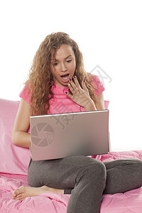 震惊的年轻女子坐在床上用笔记本电脑女性互联网技术背景图片