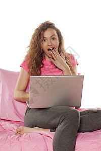 震惊的年轻女子坐在床上用笔记本电脑技术女性互联网背景图片