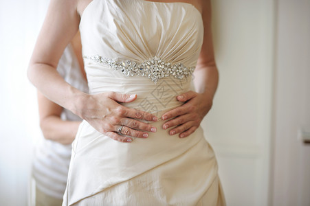 穿上婚纱时新娘的手婚礼女士衣服奢华帮助庆典裙子白色背景图片